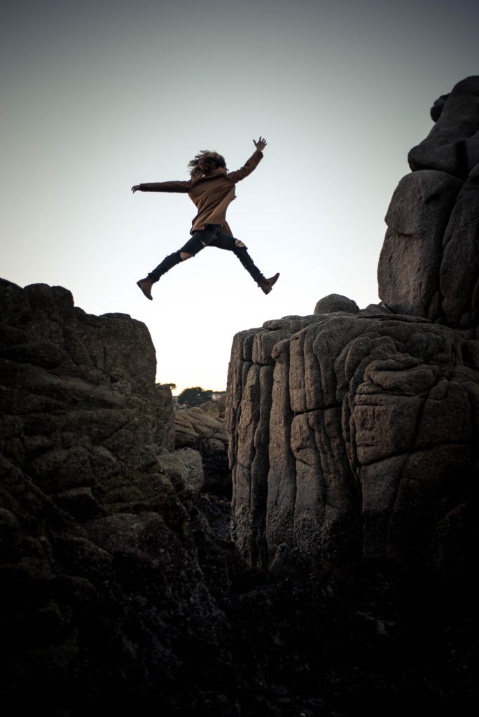 A person taking a risk and jumping from a cliff to another cliff. This represents that It is worth taking a leap of faith from time to time to reach your goals.